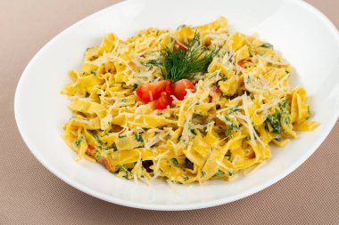 Peynirli makarna, domates ve otlar bej kumaş arka planında beyaz bir tabakta.