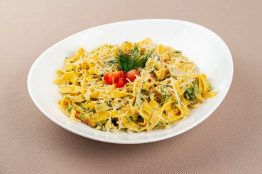 Peynirli makarna, domates ve otlar bej kumaş arka planında beyaz bir tabakta.