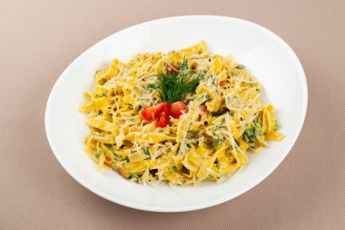 Peynirli makarna, domates ve otlar bej kumaş arka planında beyaz bir tabakta.