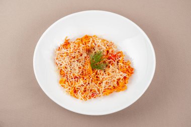domates soslu makarna, peynir, mantar ve otlar bej kumaş arka planda beyaz bir tabakta.