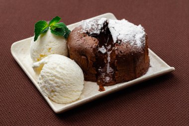 Çikolata tozu şekerle kaplanmış, iki top dondurma ve kahverengi arka planda beyaz bir tabakta nane şekeri.