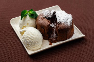 Çikolata tozu şekerle kaplanmış, iki top dondurma ve kahverengi arka planda beyaz bir tabakta nane şekeri.