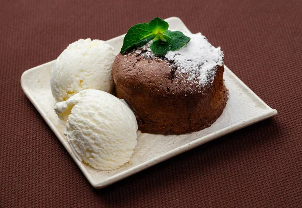 チョコレートフォンダンアイシングシュガーとアイスクリームとミントの2つのボールを茶色の背景に白いプレートに入れて — ストック写真
