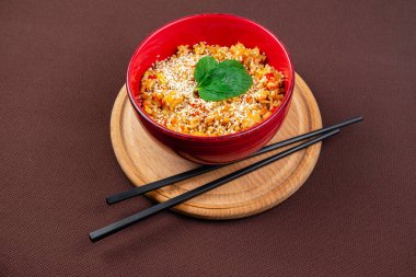 Susam tohumlu Çin pilavı, nane ve siyah ahşap çubuklar kırmızı tabakta kahverengi arka planda ahşap yuvarlak bir tahta üzerinde