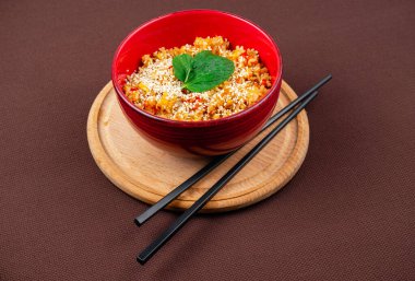 Susam tohumlu Çin pilavı, nane ve siyah ahşap çubuklar kırmızı tabakta kahverengi arka planda ahşap yuvarlak bir tahta üzerinde