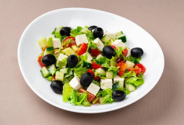 Beyaz bir tabakta bej arka planda Yunan salatası