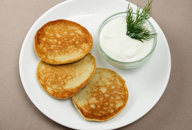 Bej arka planda beyaz bir tabakta otlu krep ve ekşi krema.