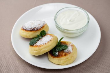 Naneli ve ekşi kremalı krep, bej arka planda beyaz yuvarlak bir tabakta cam bir tabakta.