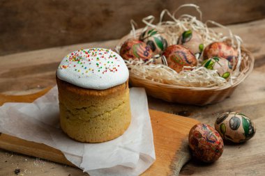 Paskalya pastası ve hasır sepetteki paskalya yumurtaları ve tahta arka planda çiçek açan bir dal.