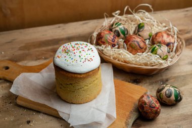 Paskalya pastası ve hasır sepetteki paskalya yumurtaları ve tahta arka planda çiçek açan bir dal.