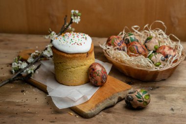Paskalya pastası ve hasır sepetteki paskalya yumurtaları ve tahta arka planda çiçek açan bir dal.