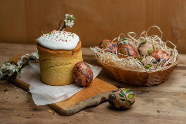 Paskalya pastası ve hasır sepetteki paskalya yumurtaları ve tahta arka planda çiçek açan bir dal.