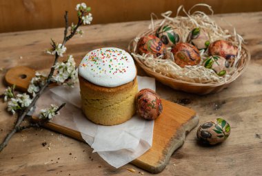 Paskalya pastası ve hasır sepetteki paskalya yumurtaları ve tahta arka planda çiçek açan bir dal.