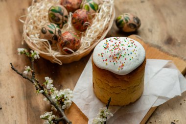 Paskalya pastası ve hasır sepetteki paskalya yumurtaları ve tahta arka planda çiçek açan bir dal.