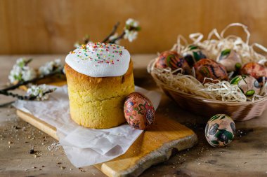 Paskalya pastası ve hasır sepetteki paskalya yumurtaları ve tahta arka planda çiçek açan bir dal.