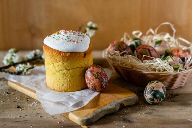 Paskalya pastası ve hasır sepetteki paskalya yumurtaları ve tahta arka planda çiçek açan bir dal.