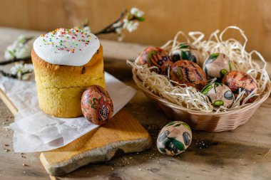 Paskalya pastası ve hasır sepetteki paskalya yumurtaları ve tahta arka planda çiçek açan bir dal.