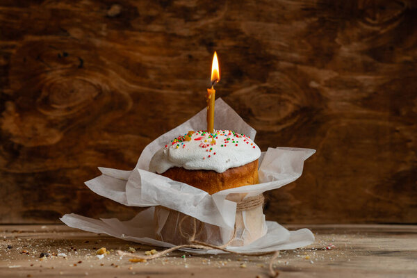 Easter cake with a burning candle in parchment paper on a wooden background