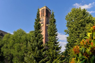Gökyüzü ve ağaçların arka planında bir saati olan tuğla kule.
