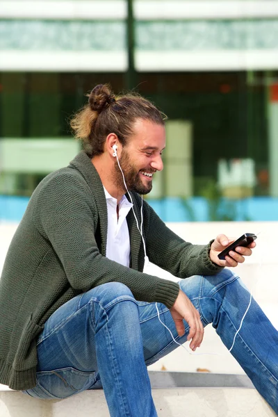 Homem sorridente sentado em degraus ouvindo música — Fotografia de Stock