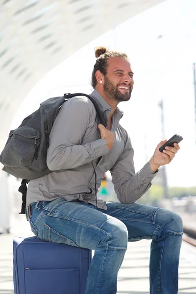 Улыбающийся мужчина сидит на чемодане с телефоном — стоковое фото