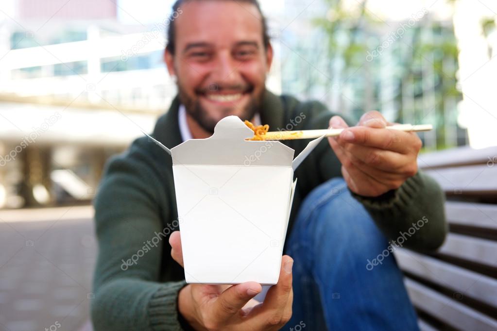 Happy man sitting and offering take out noodles