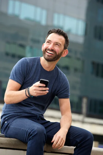 Souriant homme mature assis à l'extérieur avec téléphone intelligent — Photo