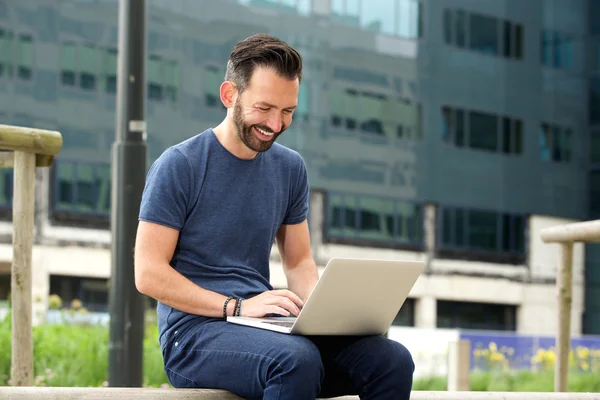 Homem alegre sentado ao ar livre e trabalhando no laptop — Fotografia de Stock