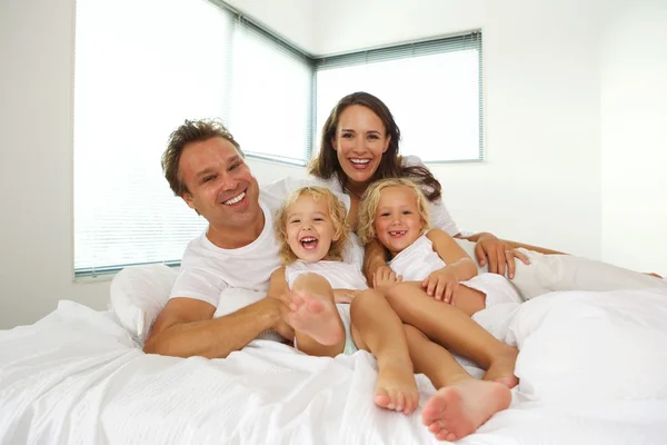 Family of four lying in bed — Stockfoto
