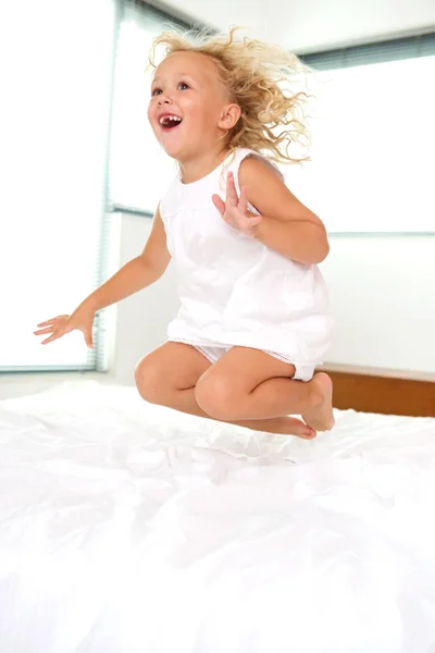 Cheerful young girl jumping on bed — Stock Photo, Image