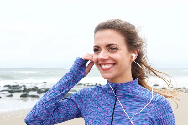 Mulher sorrindo na praia com fones de ouvido — Fotografia de Stock