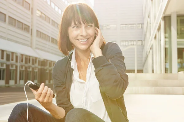 Mujer sosteniendo teléfono inteligente con auriculares — Foto de Stock