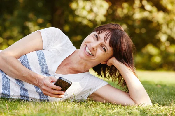 Vrouw liggend in het gras met telefoon — Stockfoto
