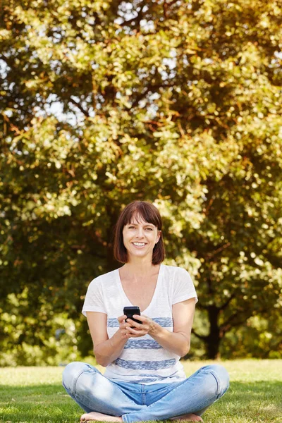 Kvinna sitter i gräset med telefon — Stockfoto