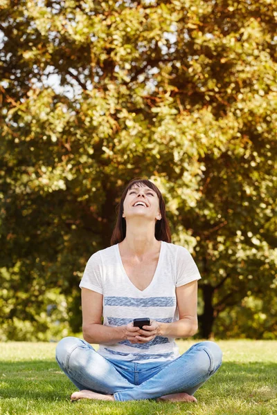 Kvinna sitter i gräset med telefon — Stockfoto