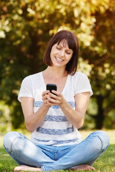 Vrouw zitten in het gras met telefoon — Stockfoto