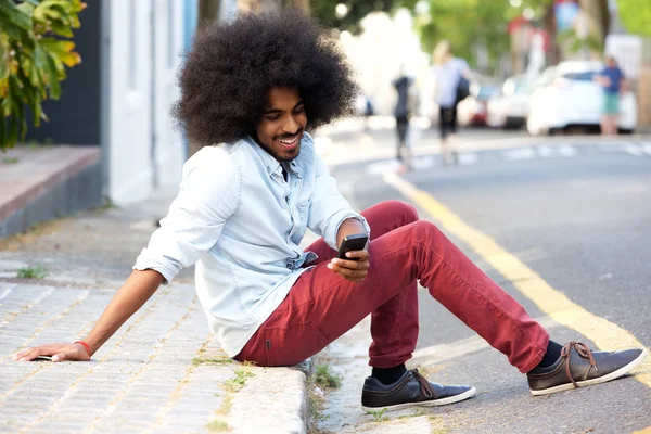 Mężczyzna z telefonu komórkowego siedzi na chodniku — Zdjęcie stockowe
