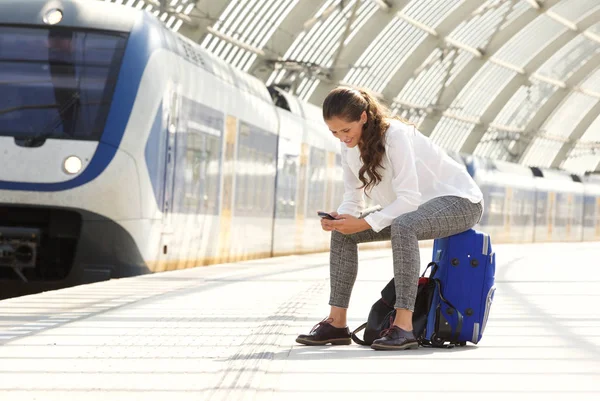 Frau sitzt mit Handy auf Koffer — Stockfoto