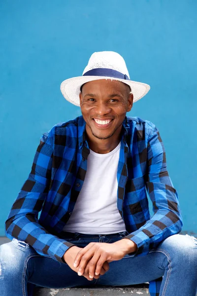 Young man with hat sitting outside and smiling — Stok fotoğraf