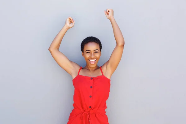 Woman smiling with arms raised against gray — Stock Photo, Image