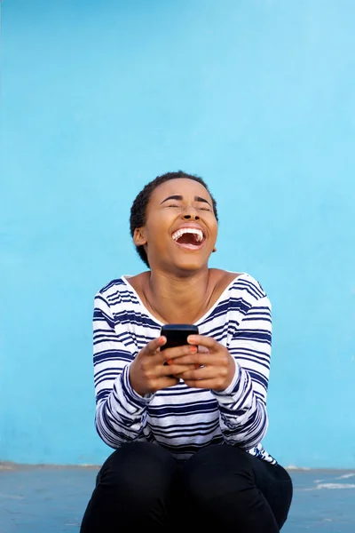 woman laughing with cell phone against wall