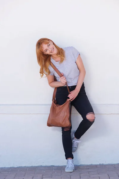 Smiling woman leaning on white wall with bag — Stock Photo, Image