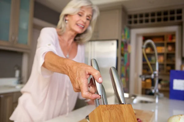 Happy older woman in kitchen with knife block — Stock Photo, Image