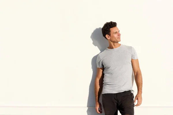 Handsome man in t-shirt standing against white wall — Stock Photo, Image