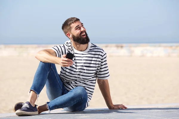 Homem em fones de ouvido sentado na praia — Fotografia de Stock