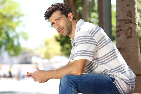 Молодий чоловік сидить на вулиці з мобільним телефоном — стокове фото
