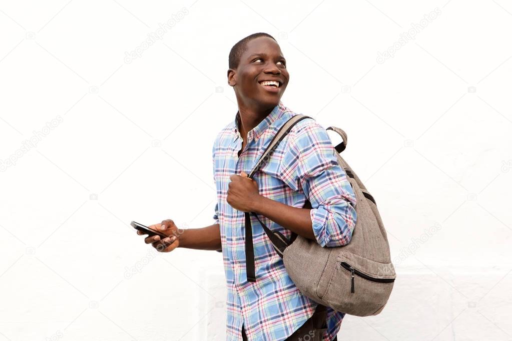 Portrait of happy young man walking with bag and mobile phone against white background