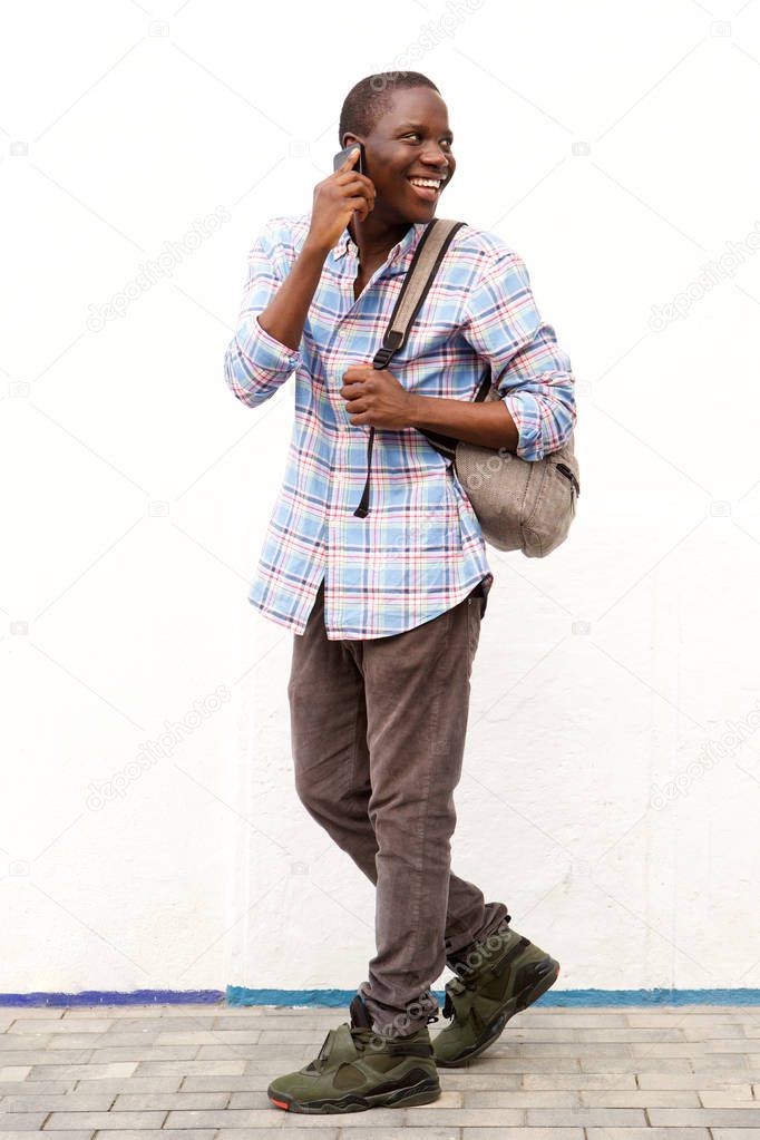Full body portrait of smiling african man walking outside and talking on cell phone