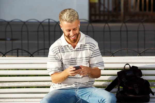 Retrato Joven Sonriente Sentado Banco Escuchando Música Teléfono Inteligente — Foto de Stock