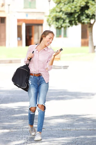 バッグ外を歩くと 携帯電話を見ていると若い女性の全身肖像画 — ストック写真